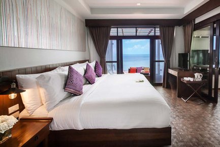 Ein elegantes Hotelzimmer mit einem großen Bett, bunten Kissen und Blick auf das Meer durch große Fenster.