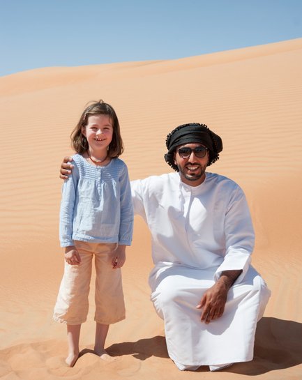 Mädchen steht neben einem Beduinen in der Wüste Omans – Oman mit Kindern