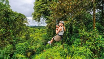 Eine Frau schwingt fröhlich an einer Zipline über üppige grüne Wälder in Costa Rica, umgeben von tropischer Vegetation.