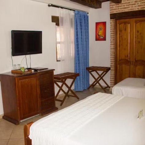 Ein gemütliches Zimmer mit zwei Betten, einem Fernseher und einem Holzschrank, umgeben von warmen Farben und natürlichem Licht.