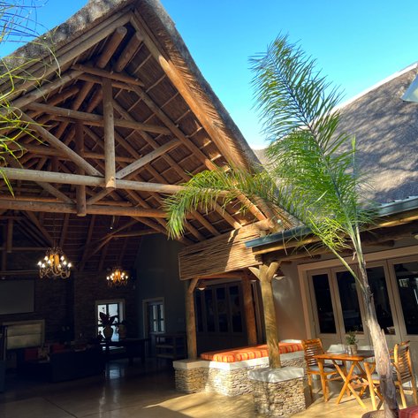 Ein einladender Innenraum mit einem hohen Strohdach, Holzsäulen und gemütlichen Sitzgelegenheiten, umgeben von Pflanzen.