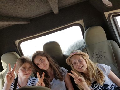 Drei Mädchen sitzen auf der Rückbank eines Jeeps und zeigen " Peace " - Namibia Urlaub mit Kindern