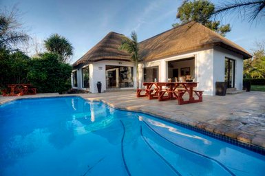 Ein einladendes Gästehaus mit Strohdach, umgeben von üppigem Grün und einem glitzernden Pool im Vordergrund.