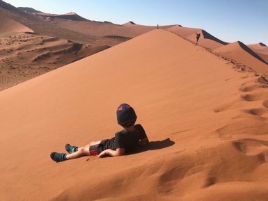 Ein Junge liegt im Sand einer Düne in der Wüste - Namibia Urlaub mit Kindern