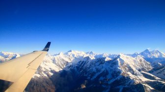 Der Blick aus dem Flugzeug zeigt majestätische schneebedeckte Berge unter einem klaren blauen Himmel.