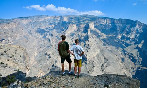 Teenager und Kind blicken gemeinsam auf die atemberaubende Schluchtlandschaft des Jebel Shams – Oman mit Kindern