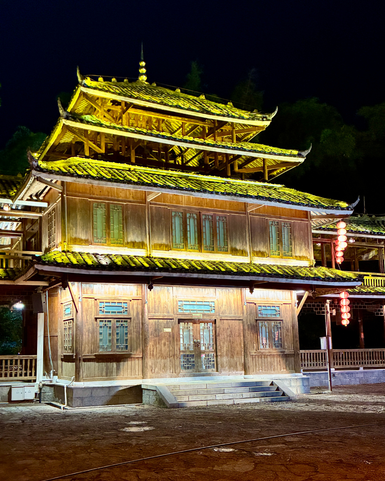 Ein traditionelles Holzgebäude mit leuchtend gelben Dächern und grünen Fenstern, beleuchtet in der Nacht.
