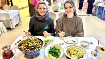 Zwei Frauen sitzen an einem Tisch in einem Restaurant, lächeln und genießen ein köstliches asiatisches Gericht.