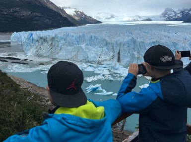 Zwei Kinder stehen an einem Aussichtspunkt und betrachten den beeindruckenden Perito-Moreno-Gletscher unter einem blauen Himmel.