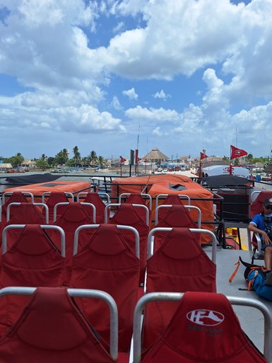 Rote Sitze auf einem Boot mit Blick auf einen Hafen, umgeben von Palmen und einem blauen Himmel mit Wolken.