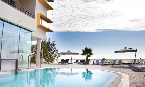 Ein glitzernder Pool spiegelt den blauen Himmel und die Wolken wider, umgeben von modernen Liegen und Sonnenschirmen.