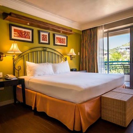 Ein helles Hotelzimmer mit einem großen Bett, umgeben von warmen Farben und Kunstwerken an der Wand.