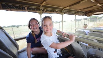 Zwei Mädchen sitzen in einem offenen Safari-Jeep und blicken in die Kamera - Namibia Urlaub mit Kindern