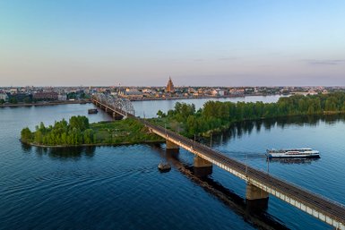 Eine beeindruckende Aussicht auf die Stadt Riga mit einer Brücke, die über den Fluss führt, umgeben von üppigem Grün.