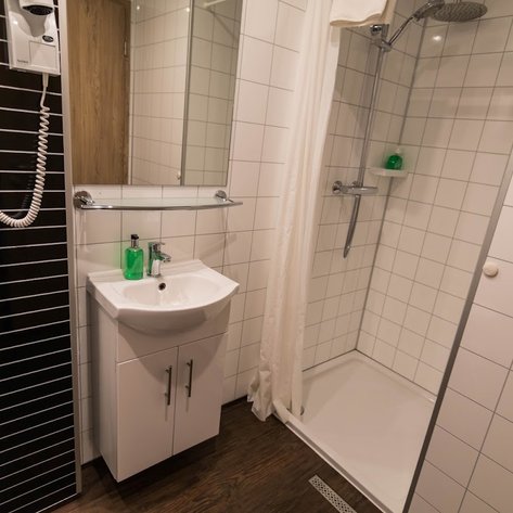 Ein modernes Badezimmer mit einer Dusche, einem Waschbecken und grünen Seifenspendern auf einem weißen Fliesenboden.