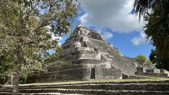 Eine beeindruckende Maya-Pyramide erhebt sich majestätisch unter einem klaren blauen Himmel mit einigen Wolken.