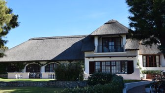 Ein charmantes Haus mit einem Reetdach, umgeben von gepflegten Gärten und einem klaren blauen Himmel.