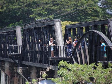 Eine Gruppe von Touristen steht auf einer historischen Brücke, umgeben von üppigem Grün und einem ruhigen Fluss.