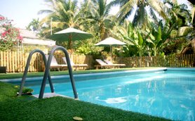 Ein einladender Pool umgeben von üppigem Grün und Palmen, mit Liegen und Sonnenschirmen im Hintergrund.