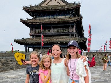 Vier Mädchen stehen fröhlich vor einem historischen Torturm in Xi'an und lächeln in die Kamera, während bunte Laternen im Hintergrund schweben.