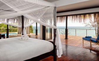 Ein luxuriöses Schlafzimmer mit einem großen Bett, umgeben von einem Moskitonetz und Blick auf das Meer durch große Fenster.