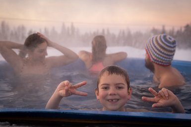 Ein fröhlicher Junge zeigt das Peace-Zeichen, während er in einem heißen Whirlpool mit Freunden entspannt.
