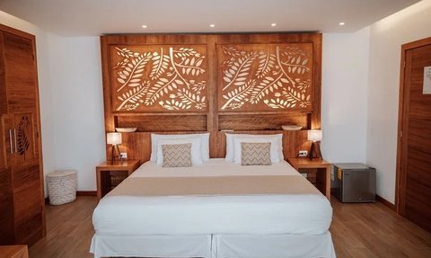 Ein stilvolles Hotelzimmer mit einem großen Doppelbett und kunstvoll geschnitztem Holzpaneel im Hintergrund.