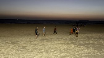 Am Strand spielen mehrere Kinder Fußball, während die Dämmerung über dem Meer leuchtet und die Wellen sanft plätschern.