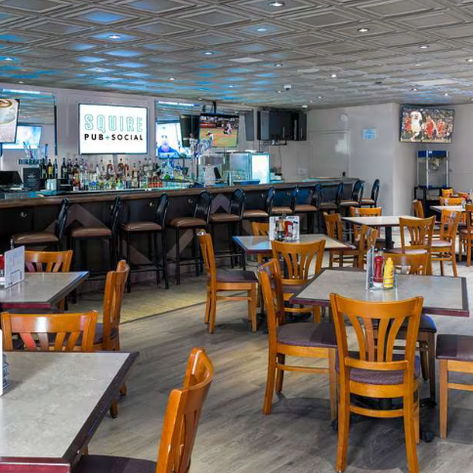 Ein einladendes Restaurant mit Holztischen und Stühlen, das eine Bar mit einer Auswahl an Getränken im Hintergrund zeigt.