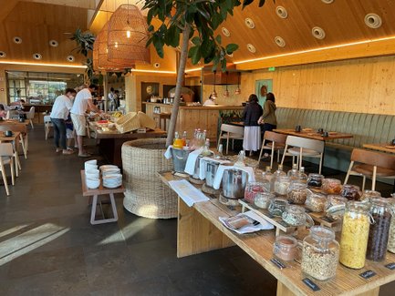 Ein modernes Restaurant mit Holzdekor, in dem Gäste an einem Buffet mit verschiedenen Lebensmitteln stehen.