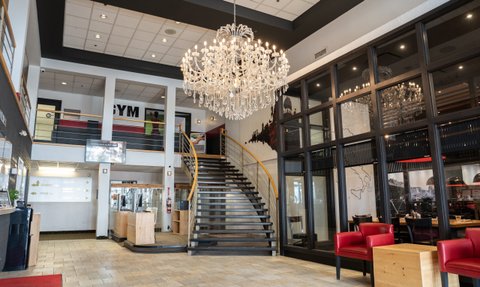 Der Empfangsbereich eines modernen Hotels mit einer eleganten Kristallleuchte und einer geschwungenen Treppe im Hintergrund.