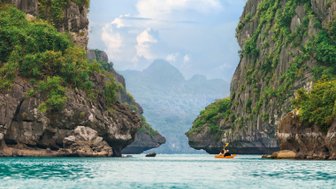 Ein Kajakfahrer paddelt durch die ruhigen Gewässer von Halong Bay, umgeben von beeindruckenden Felsen und üppiger Vegetation.