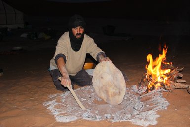 Beduine backt traditionelles Fladenbrot direkt auf dem Wüstensand – Marokko Familienreise