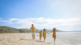 Eine fröhliche Familie in gelben Outfits läuft am Strand entlang, während die Wellen sanft ans Ufer schlagen.
