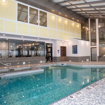 Ein moderner Innenpool mit glitzerndem Wasser, umgeben von hellen Wänden und großen Fenstern, die Tageslicht hereinlassen.