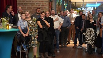 Eine Gruppe von Menschen steht in einem modernen Raum, einige lächeln, während sie auf eine Präsentation warten.