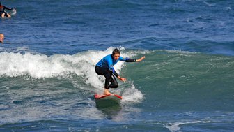 Eine Surferin in einem blauen Neoprenanzug reitet auf einer Welle und zeigt Geschicklichkeit und Balance.