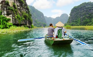 Zwei Personen sitzen in einem Boot und genießen die ruhige Landschaft mit hohen, bewaldeten Klippen im Hintergrund.