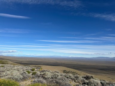 Eine weite, offene Landschaft in Patagonien, mit sanften Hügeln und einem strahlend blauen Himmel voller Wolken.