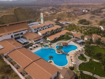 Ein weitläufiges Resort mit einem großen Pool, umgeben von Palmen und Sonnenliegen, in einer sonnigen Landschaft.