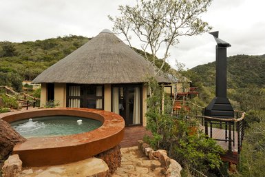 Ein traditionelles Rundhaus mit einem Strohdach, umgeben von üppiger Natur und einem kleinen Whirlpool im Vordergrund.