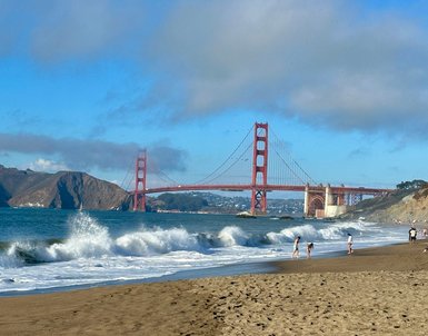 Am Strand von San Francisco spielen Kinder im Wasser, während die Golden Gate Bridge majestätisch im Hintergrund thront.