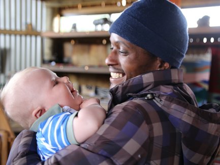 Einheimischer trägt lächelnd ein Baby auf dem Arm – Südafrika Familienreise
