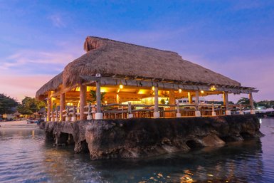 Ein malerisches Pavillon am Wasser, umgeben von sanften Wellen und einem farbenfrohen Sonnenuntergang.