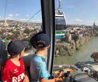 Zwei Kinder in einer Seilbahn blicken auf die Stadt und den Fluss, während sie die Aussicht genießen und spielen.