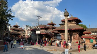 Ein belebter Platz in Kathmandu mit historischen Tempeln, Menschen, die sich versammeln, und einer beeindruckenden Wolkenformation.