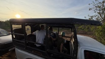 Ein Sonnenuntergang beleuchtet die Landschaft, während eine Familie in einem offenen Geländewagen sitzt und die Aussicht genießt.