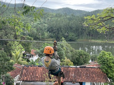 Ein Abenteurer schwingt an einem Seil über eine malerische Landschaft mit Bergen und einem ruhigen See im Hintergrund.
