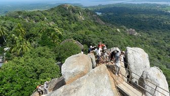 Menschen überqueren eine schmale Brücke mit Blick auf den imposanten Sigiriya-Felsen – Sri Lanka Familienreise