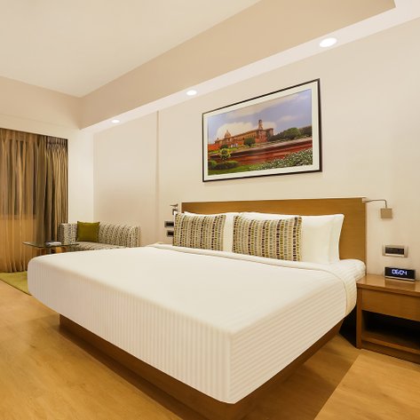 Ein modernes Hotelzimmer mit einem großen Bett, bunten Kissen und einem stilvollen Sessel in der Ecke.